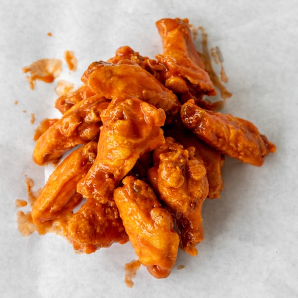 A pile of buffalo chicken wings coated in a vibrant orange sauce on white parchment paper.