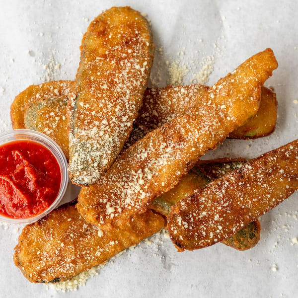 Golden-brown fried zucchini sticks, sprinkled with Parmesan cheese, served with a side of marinara sauce.