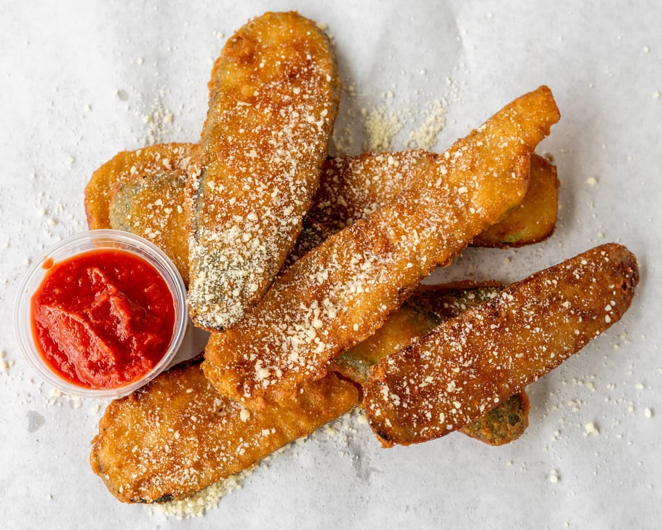 Golden-brown fried zucchini sticks, sprinkled with Parmesan cheese, served with a side of marinara sauce.