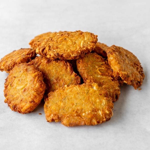 Pile of golden-brown fried zucchini fritters on a white surface.