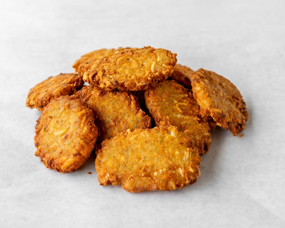 Pile of golden-brown fried zucchini fritters on a white surface.