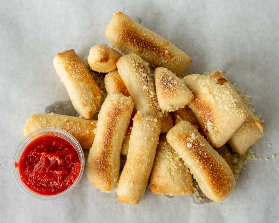 Golden-brown breadsticks, sprinkled with Parmesan cheese, served with a side of marinara sauce.