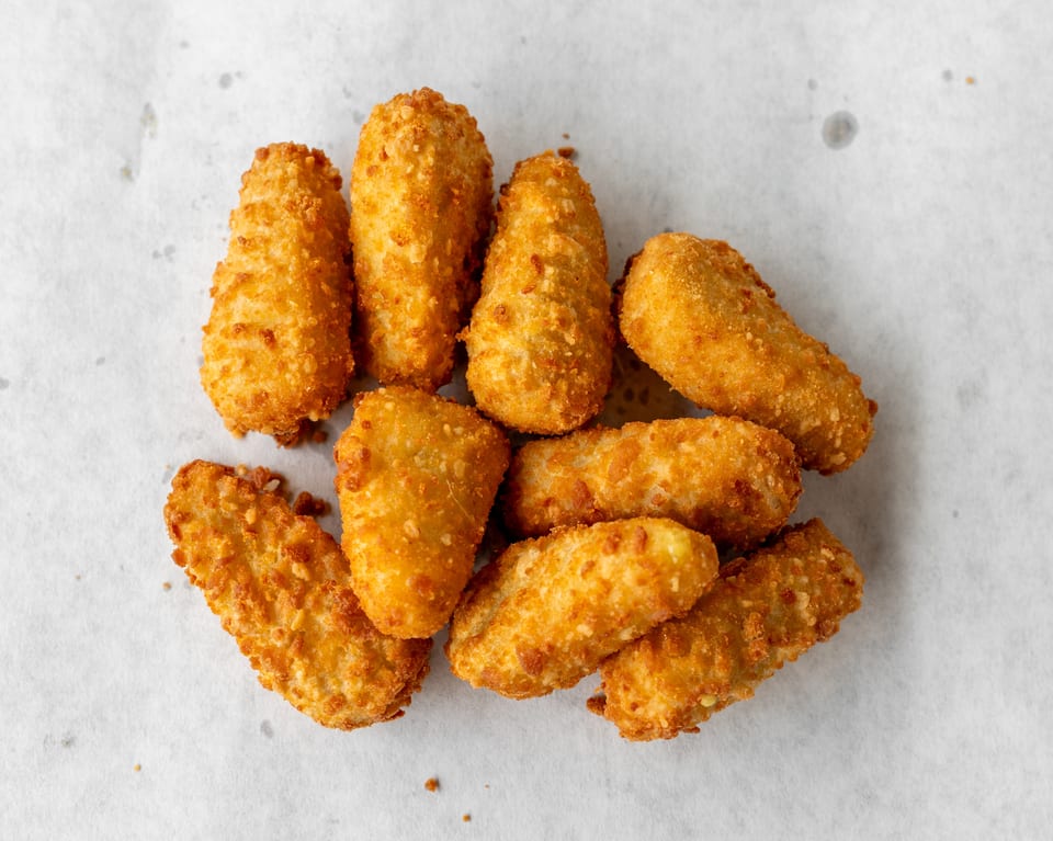 A pile of golden-brown, breaded fried cheese sticks on a white paper background.
