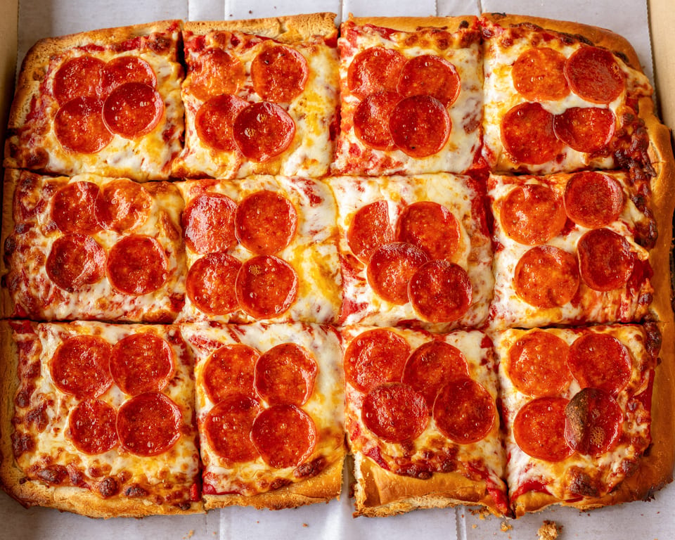 Close-up of a Detroit-style pepperoni pizza, cut into square slices, in a white box.