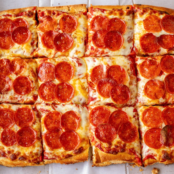 Close-up of a Detroit-style pepperoni pizza, cut into square slices, in a white box.