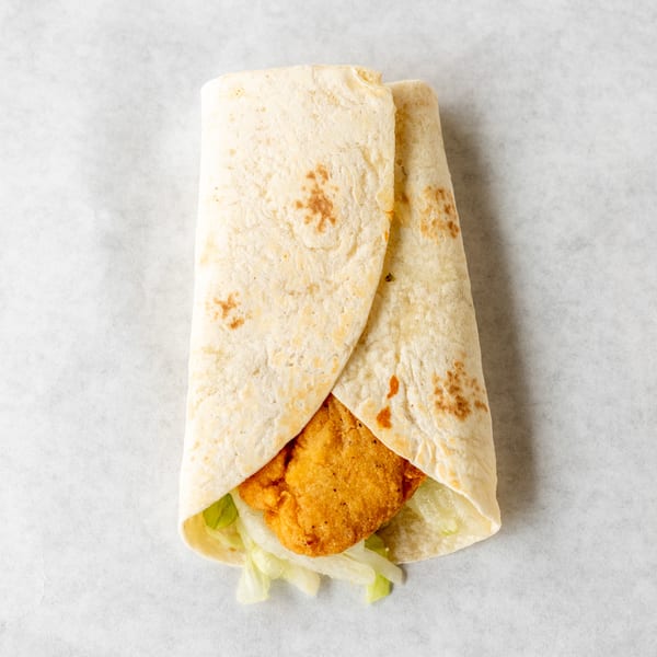 Crispy chicken tender and shredded lettuce wrapped in a soft flour tortilla on white parchment paper.