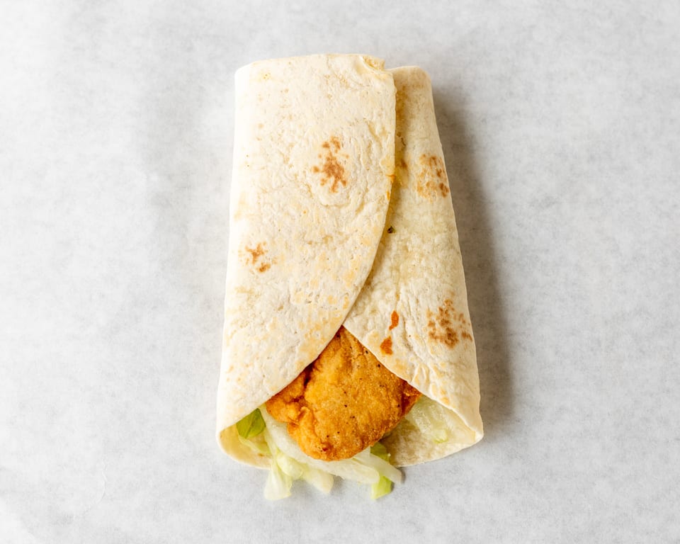Crispy chicken tender and shredded lettuce wrapped in a soft flour tortilla on white parchment paper.