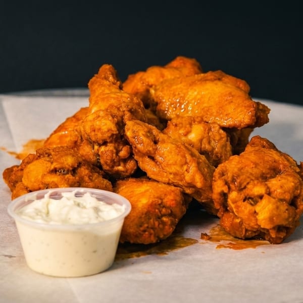 A pile of buffalo chicken wings with a side of ranch dressing on white parchment paper.