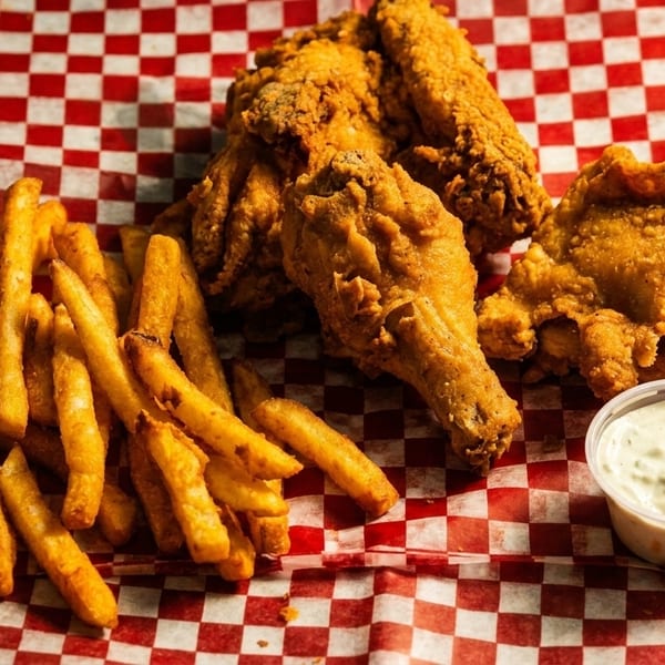 Crispy fried chicken pieces and golden french fries with a side of dipping sauce on red and white checkered paper.