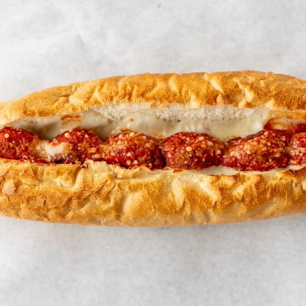Meatball sub sandwich with melted cheese and marinara sauce on a white background.