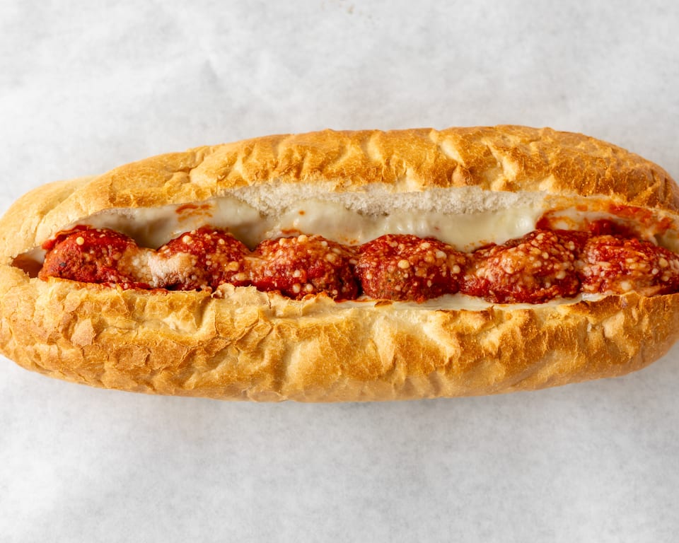 Meatball sub sandwich with melted cheese and marinara sauce on a white background.